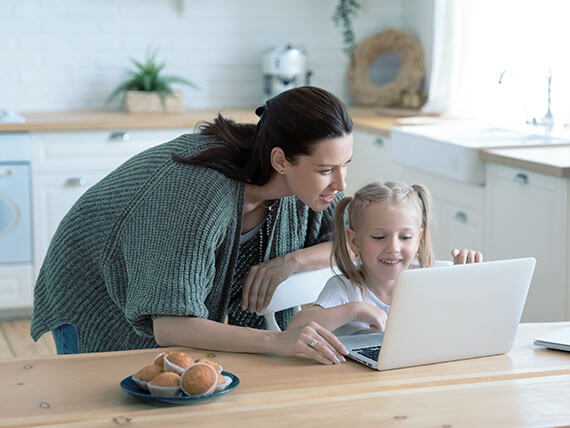 Woman assisting a small child on a laptop in the kitchen