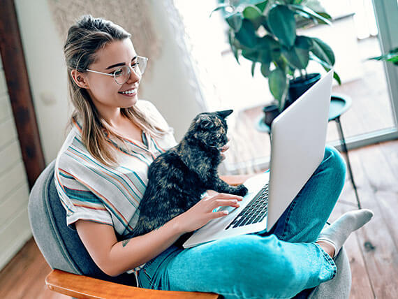 Smiling young woman sitting in a chair with her cat and laptop