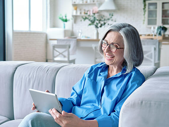 Smiling middle aged woman sitting on couch watching a tablet