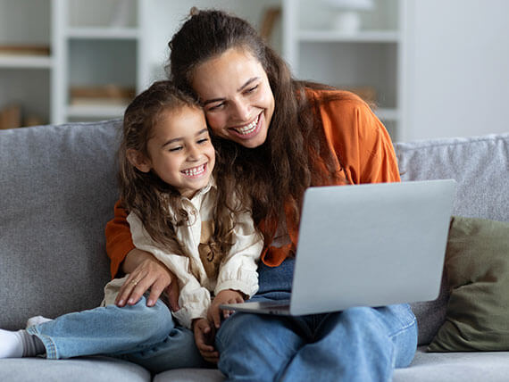 Smiling woman and child sitting on a couch viewing a laptop